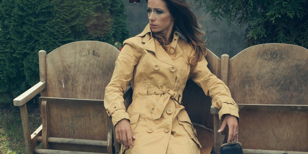 a woman in a trench coat sitting on a bench